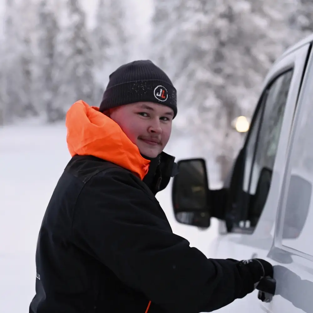 Nuori mies avaa valkoisen pakettiauton ovea lumisessa maisemassa, valmiina kiinteistöpalvelutehtäviin.